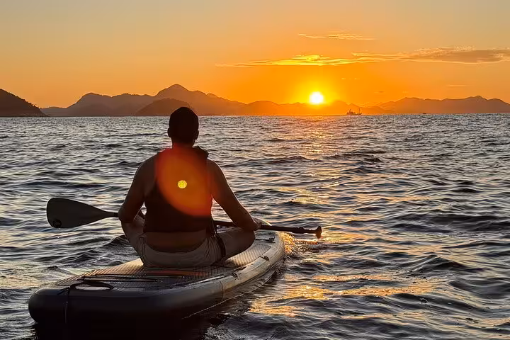 Man seated on a paddleboard witnessing a breathtaking sunrise over Copacabana's serene waters, perfect for SUP enthusiasts.