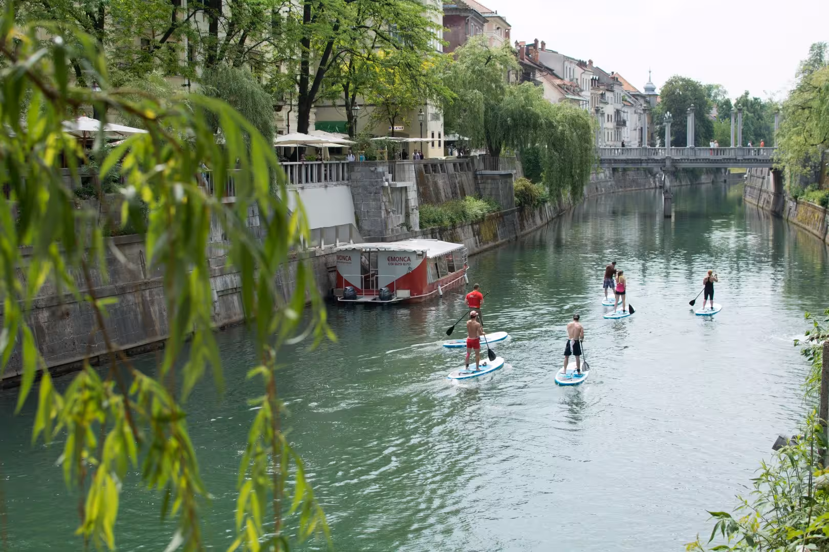 Stand up paddleboarding on Ljubljana River past riverside cafes and bridges in green city center Slovenia