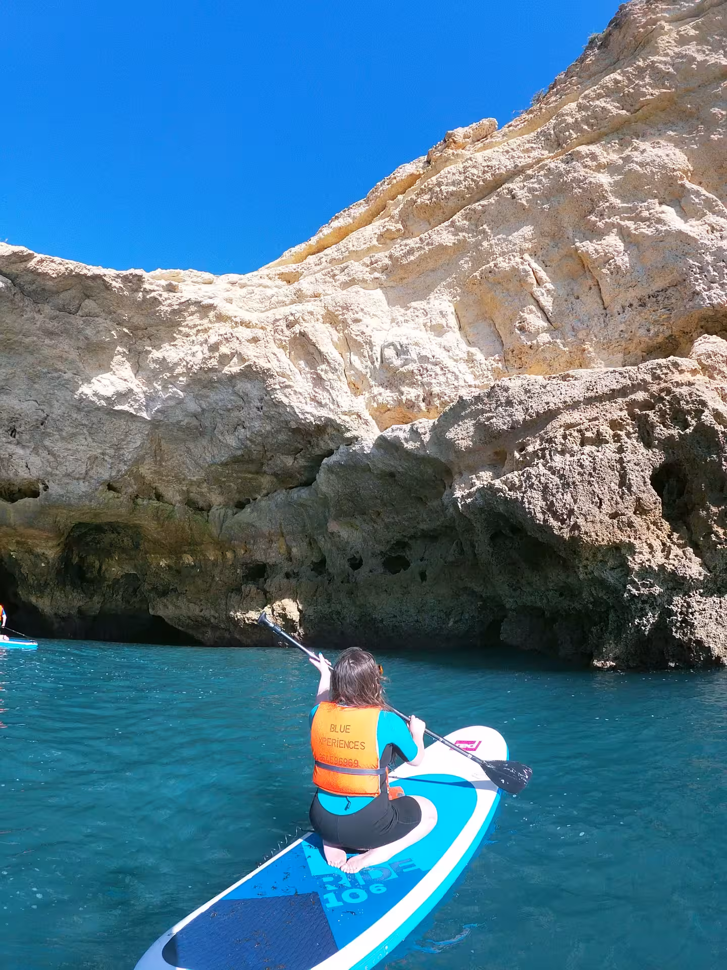 Paddler on a stand up paddle board gliding toward rugged Algarve rock formations and sea caves on a guided SUP rental