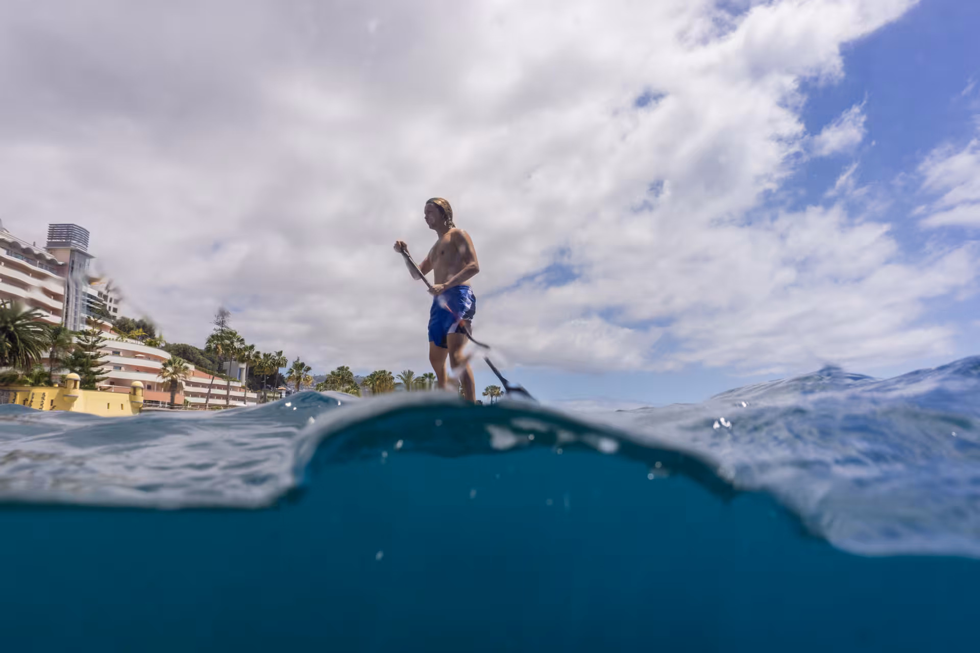 Paddleboarder exploring coastal waters with snorkeling gear under cloudy skies.