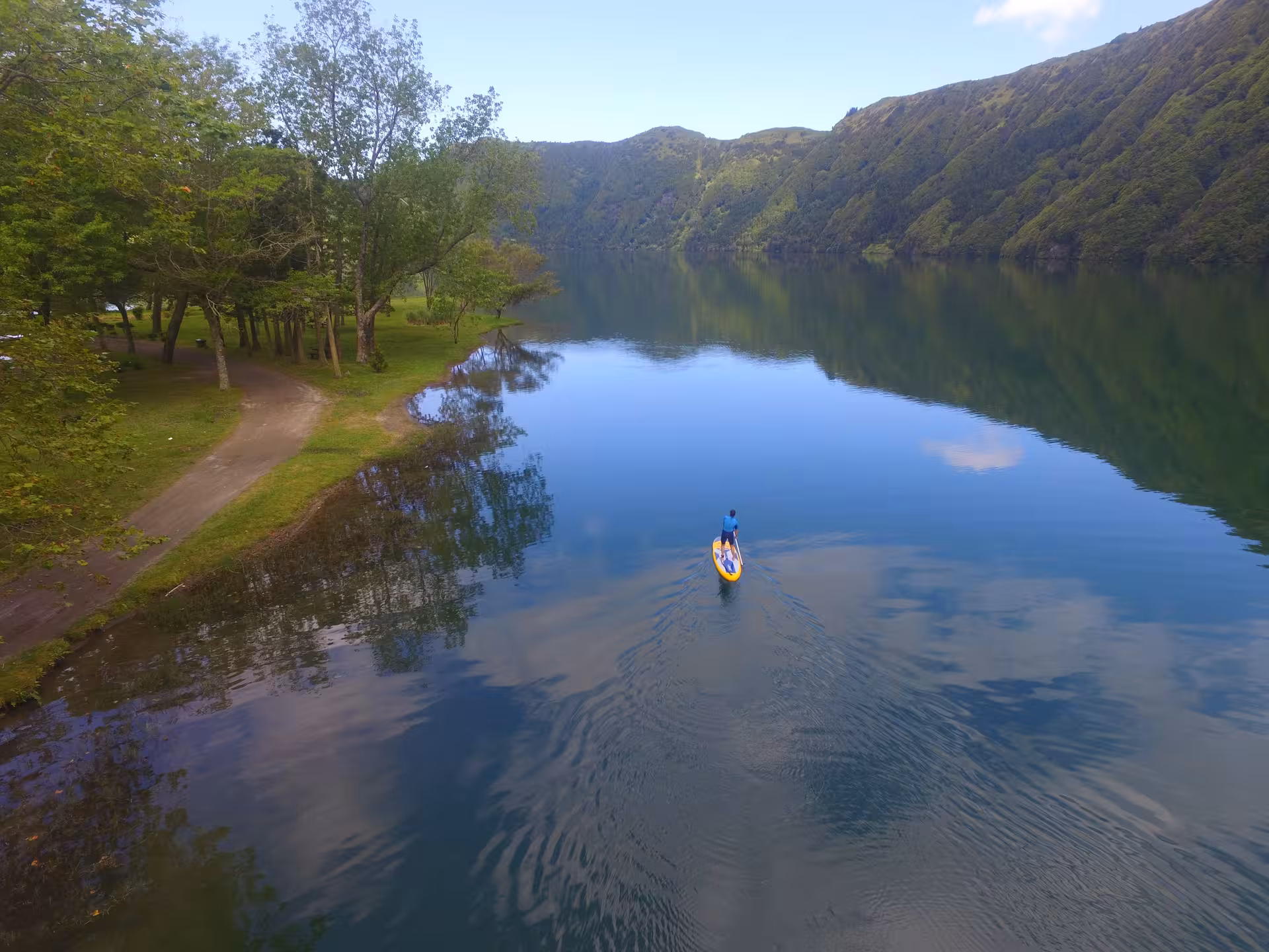 Solo paddler enjoying SUP rental on the calm blue waters of Sete Cidades lagoon, surrounded by lush green crater hills
