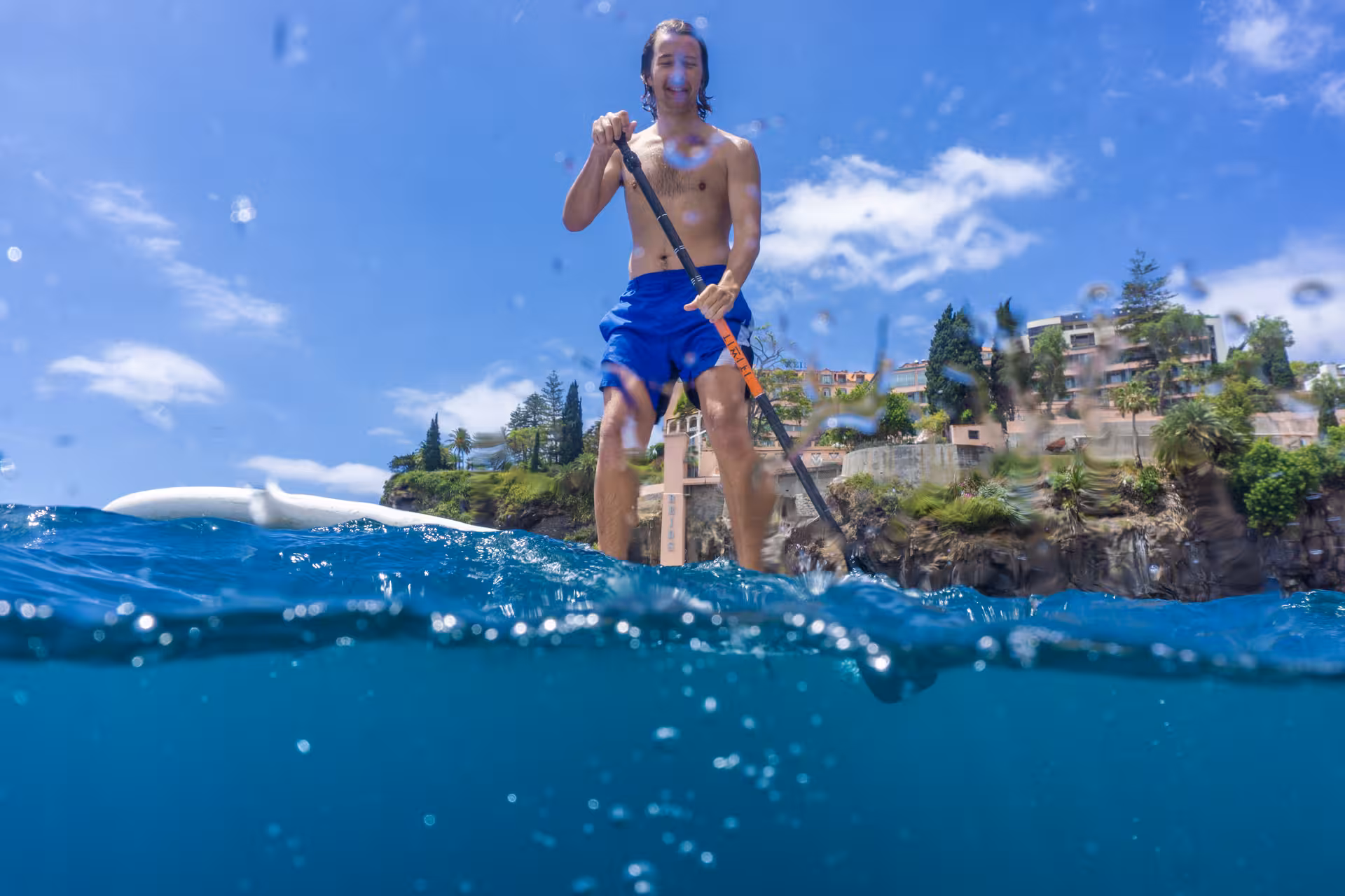 Man enjoying SUP adventure with snorkeling near scenic cliffs under blue skies.