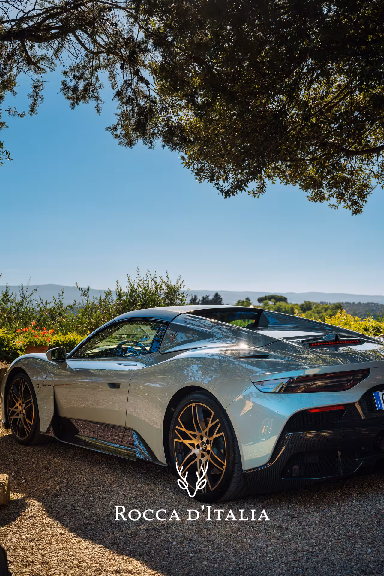 A sleek supercar parked under a tree with stunning Tuscan countryside views, perfect for a luxury driving adventure.