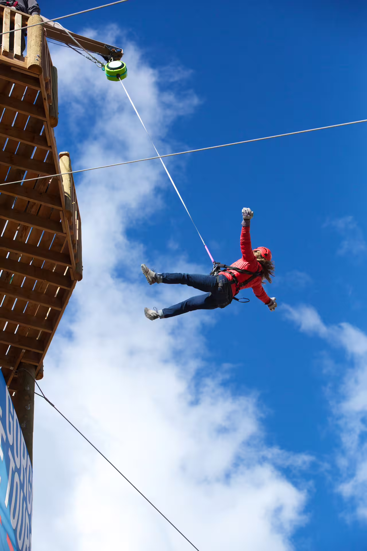 Person soaring through the sky on a zipline adventure, embodying the thrill of the Superman Ride against a bright blue sky.