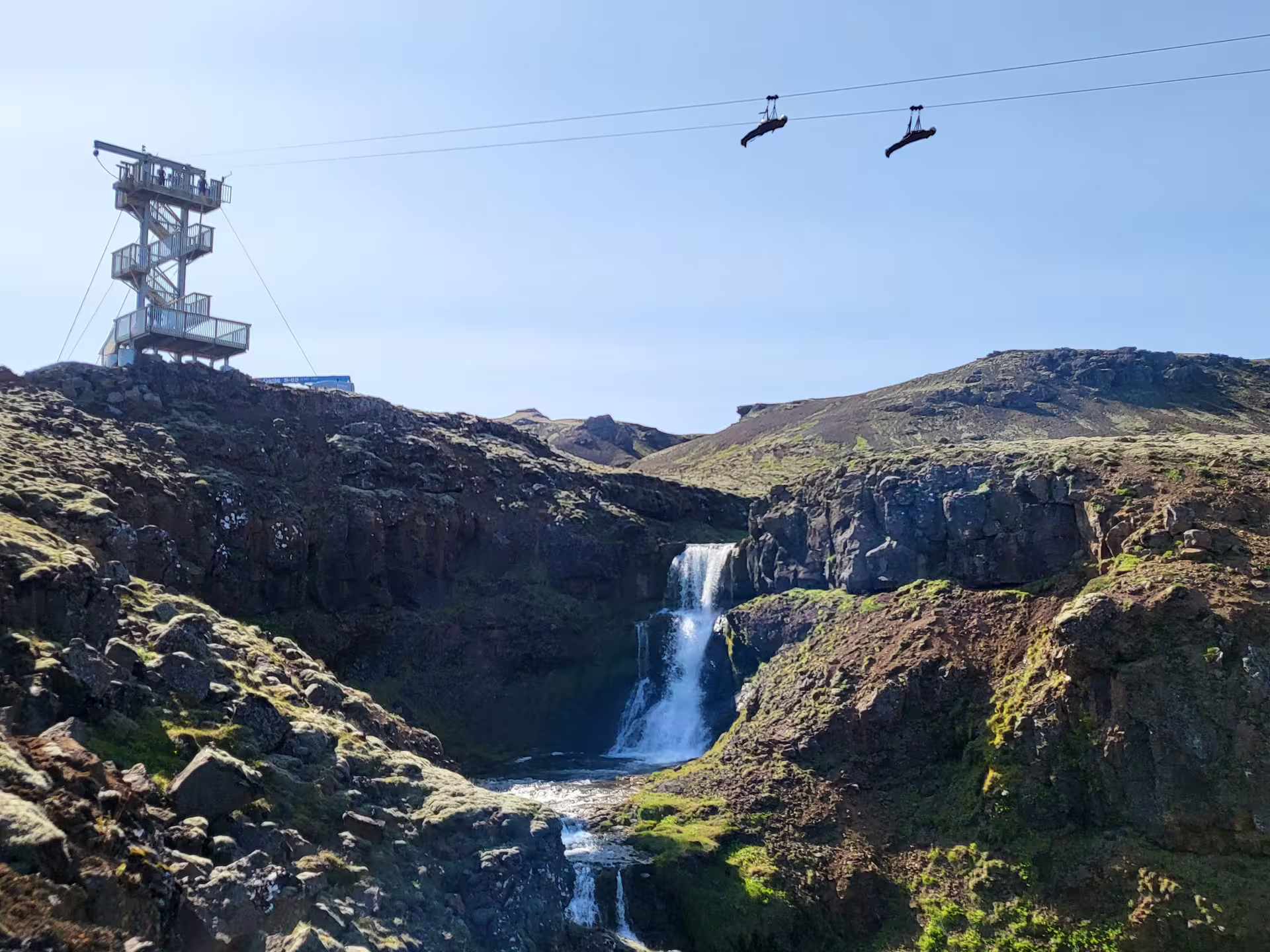 Thrill-seekers zipline over a stunning waterfall landscape on the Superman Ride, offering a breathtaking aerial adventure.