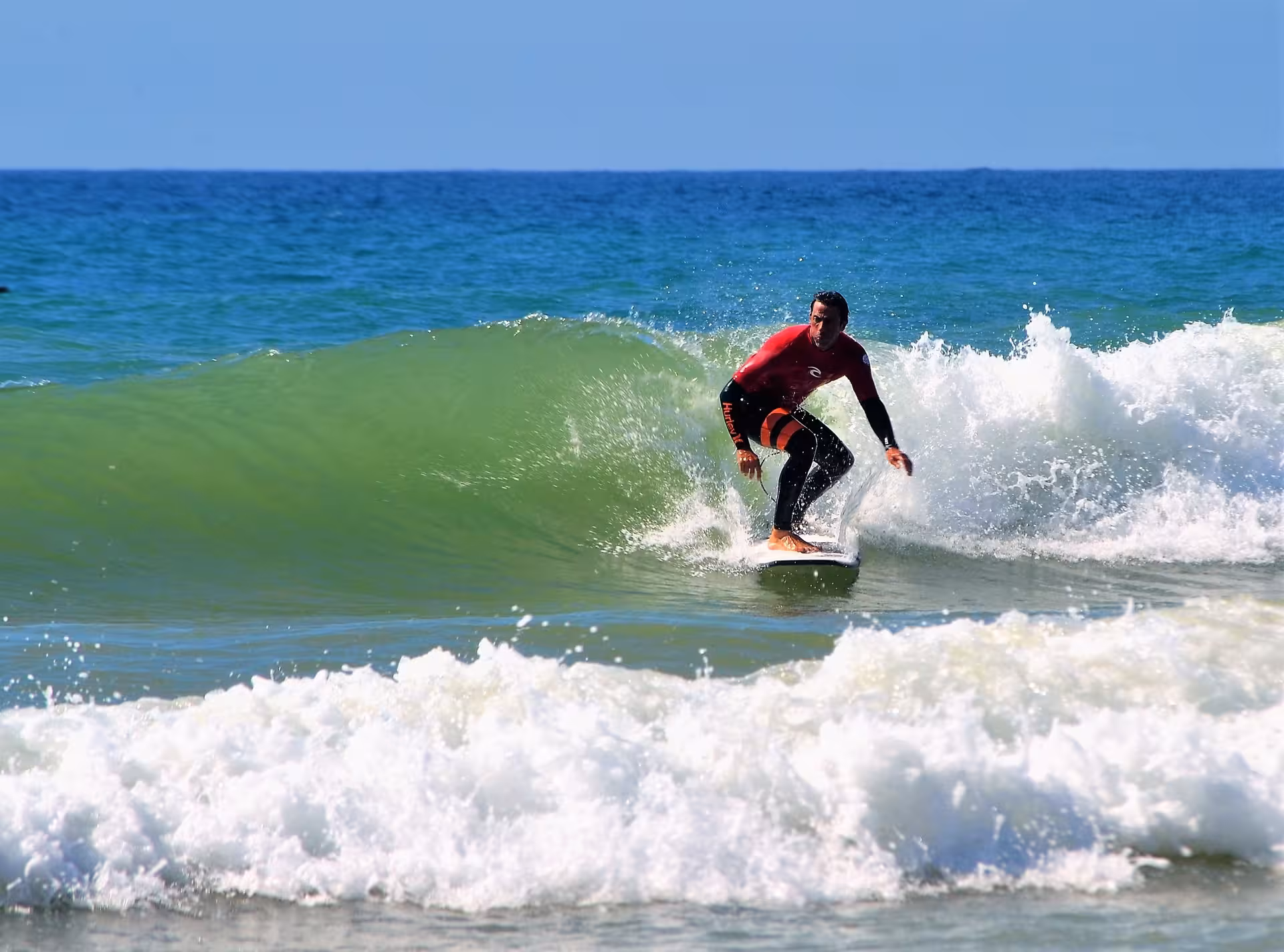 Expert surf instructor in red wetsuit skillfully riding a green wave on a full-day surfing tour in Aljezur