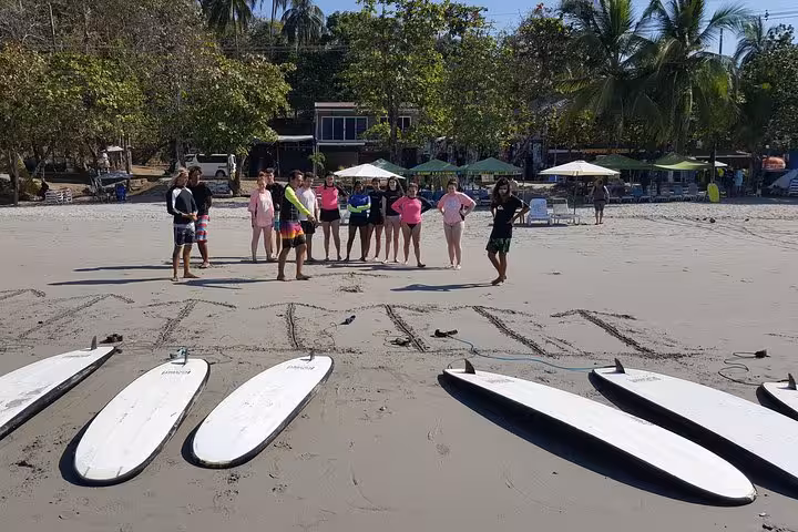 Surfboards lined up on Manuel Antonio Beach with a group preparing for a surf lesson under the tropical sun.