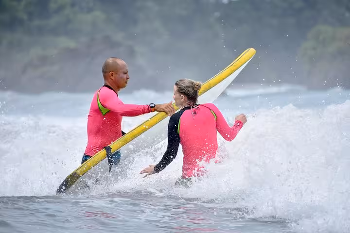 Instructor teaching a beginner to surf in the waves at Manuel Antonio, Costa Rica, wearing matching pink rash guards.