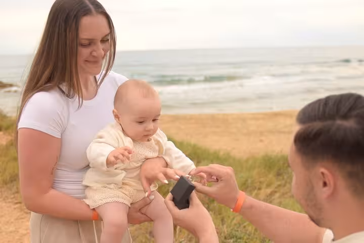 A couple with a baby experiences a surprise engagement by the sea in Hersonissos, capturing a heartfelt family moment.
