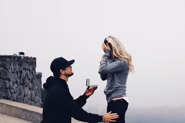 Surprise proposal photo shoot in Barcelona as man kneels with ring box by scenic stone viewpoint