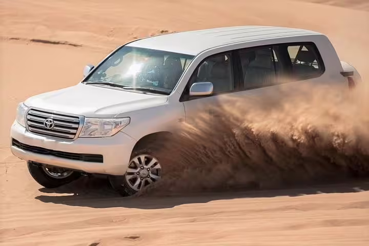 SUV kicking up sand as it powers through desert terrain in exciting dune bashing experience.