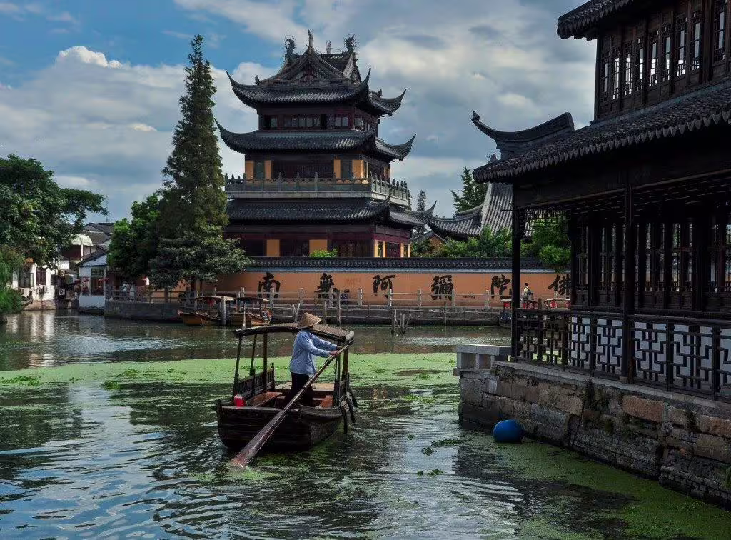 Traditional boat on Suzhou canal with historic pagoda and ancient architecture, showcasing China's cultural heritage.