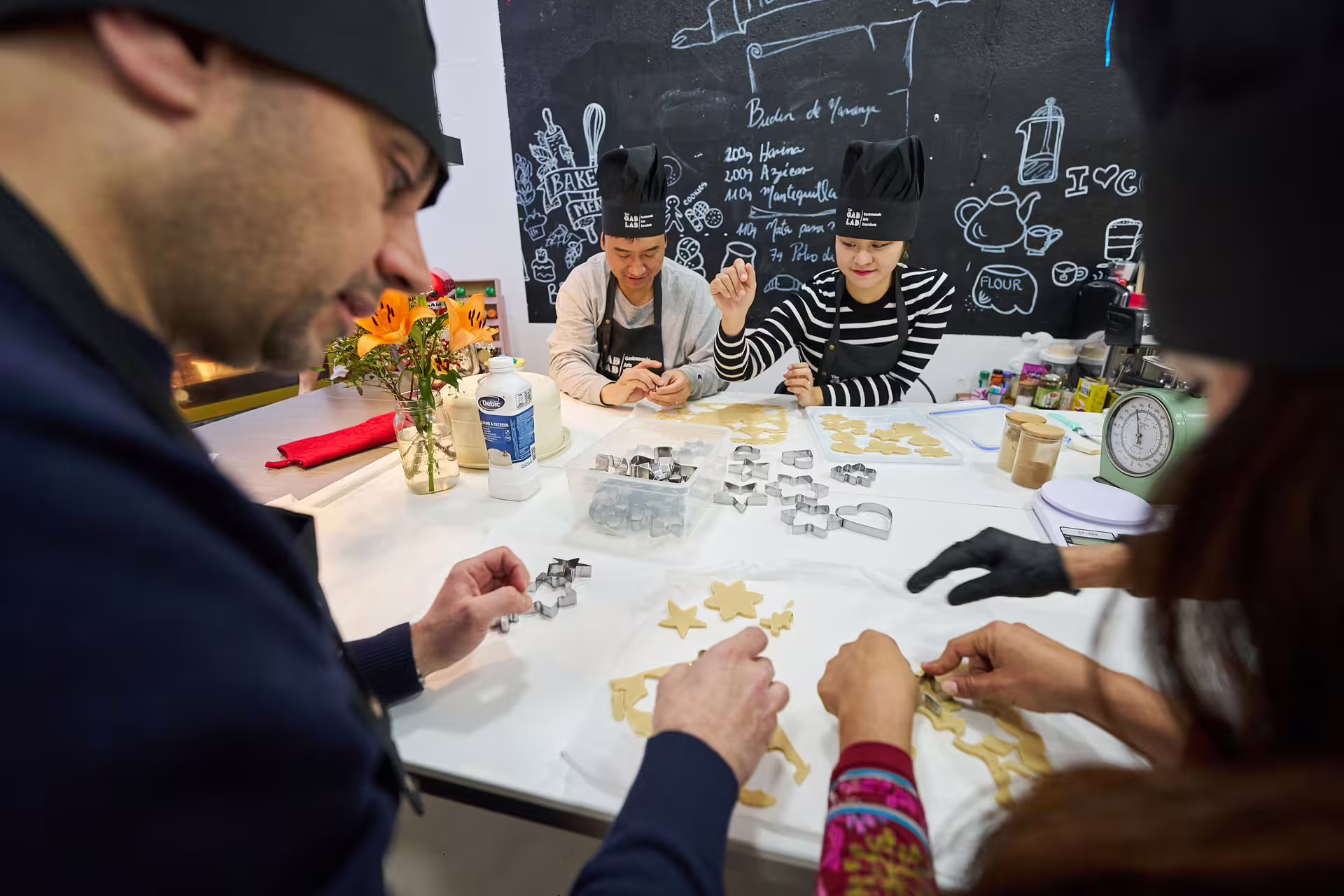 Participants crafting cookies with various cutters in a lively Sweet Escape: Bake & Take Workshop, surrounded by baking essentials.