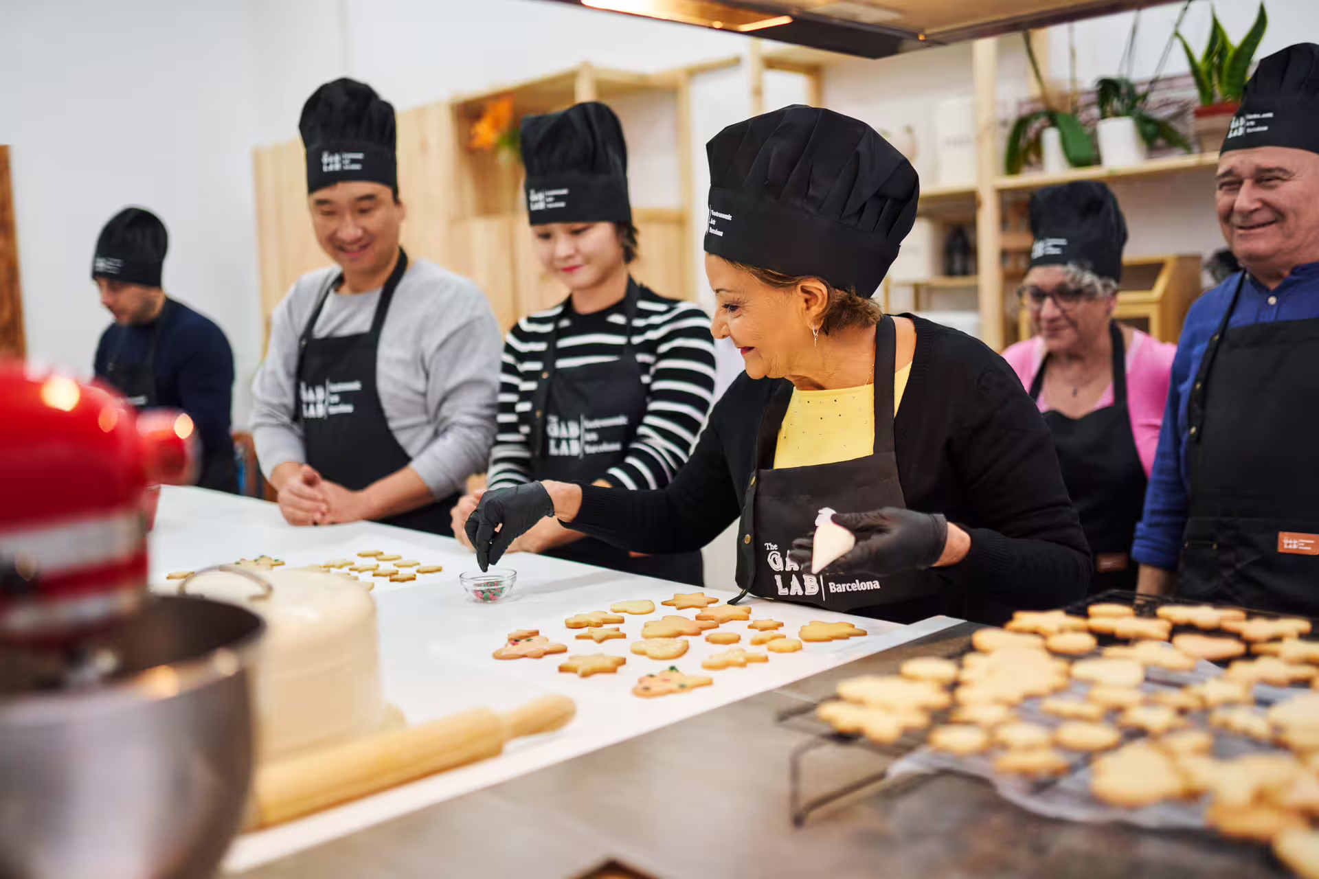 Participants enjoy hands-on baking at the Sweet Escape workshop, decorating cookies with vibrant icing in a lively kitchen setting.