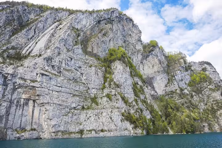 Majestic rock cliffs rising above a serene lake in the Swiss Alps, perfect for picturesque train and boat journeys.