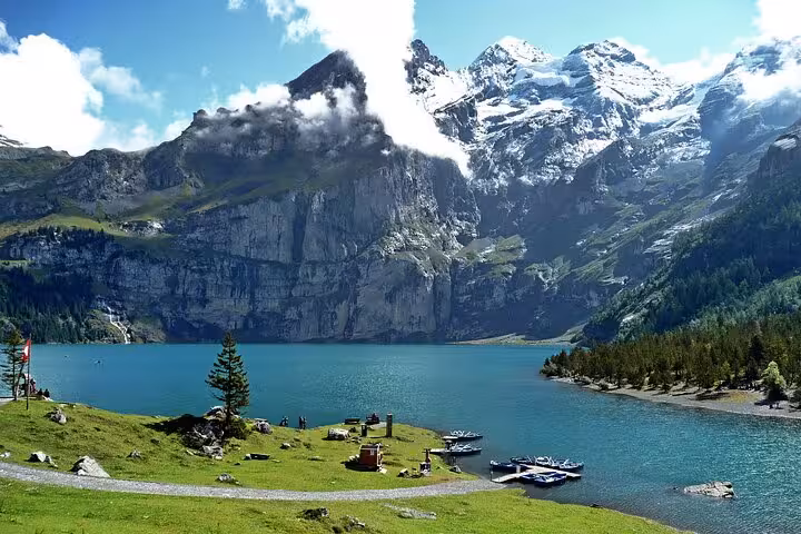 Stunning view of a turquoise lake surrounded by lush greenery and snow-capped peaks in the Swiss Alps.