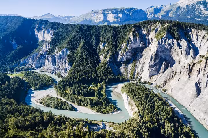 Aerial view of the Swiss Alps with a winding turquoise river surrounded by lush greenery and dramatic cliffs.