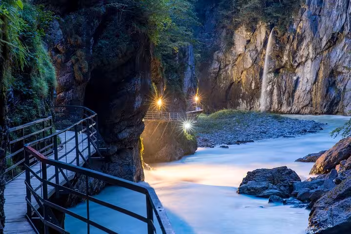 Enchanting gorge pathway with a waterfall and illuminated rocks in Swiss Alps, highlighting natural beauty for tours.