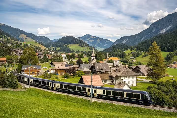Scenic Swiss train traveling through quaint alpine village with stunning mountain backdrop, perfect for rail fans.