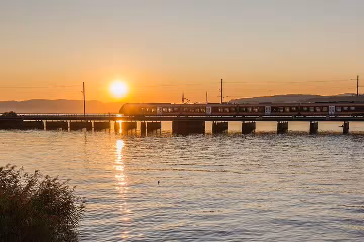 Train crossing a serene lake at sunset on the Swiss scenic express tour for train aficionados.