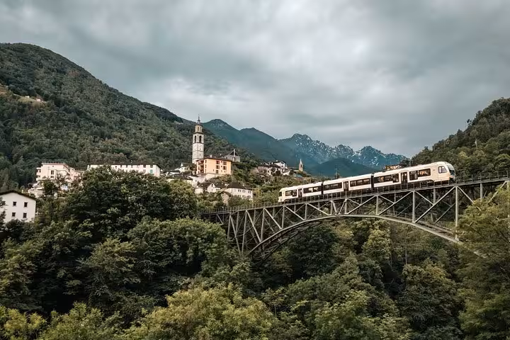 Swiss train on a steel bridge with picturesque village and mountain backdrop, a must-see for train aficionados.