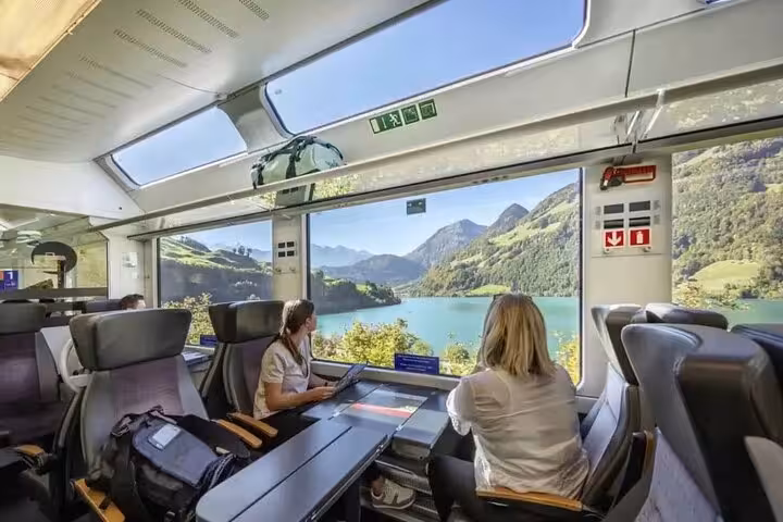 Passengers enjoying panoramic views of Swiss lakes and mountains from scenic express train.