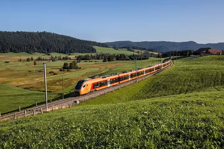 Orange Swiss train traversing lush green hills on the scenic express route for train enthusiasts.