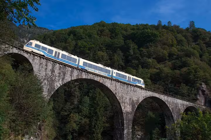 Swiss scenic train crossing a historic stone viaduct amidst lush green hills, ideal for railway adventure seekers.