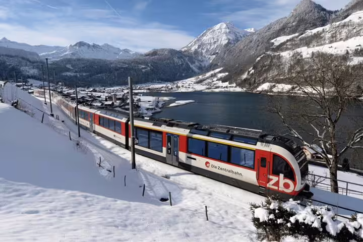 Scenic Swiss train journey through snow-capped mountains and a tranquil lake, perfect for panoramic winter travel.