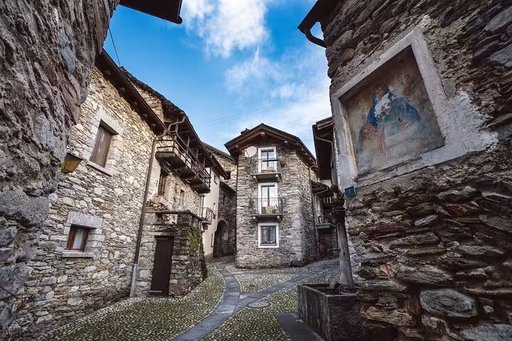 Charming cobblestone street in a historic Swiss village with rustic stone buildings under a bright blue sky.