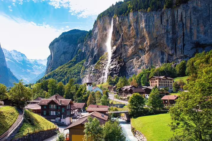 Charming Swiss village with a waterfall cascading down a cliff, seen on panoramic train journey through Switzerland.