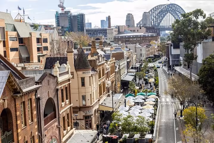 Historic Rocks district in Sydney with bustling streets and a view of the Harbour Bridge.