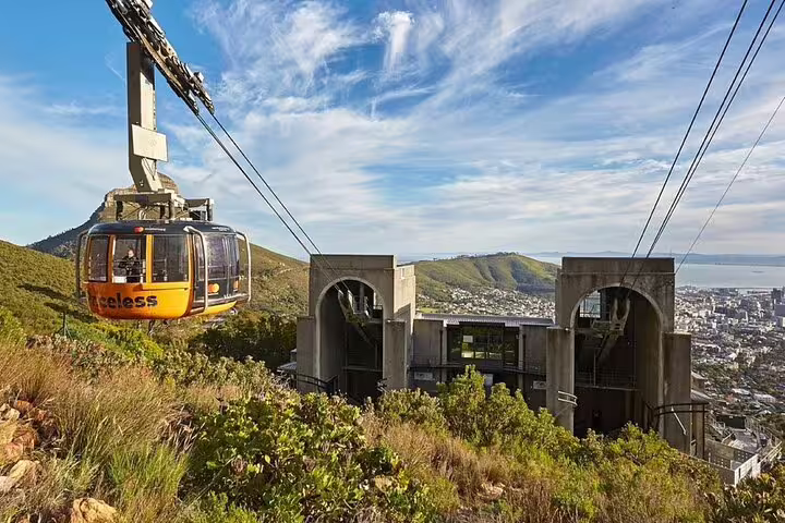 Scenic view of a cable car ascending Table Mountain against a rugged cliff backdrop in Cape Town, South Africa.