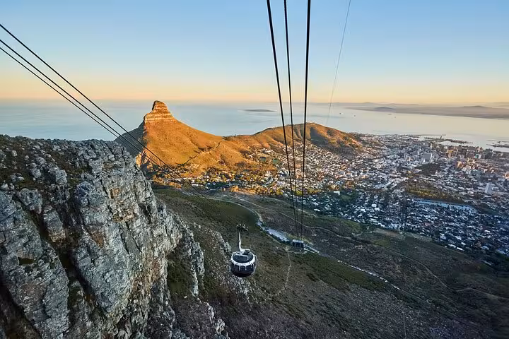 Panoramic view of Table Mountain cable car ascending with Cape Town and ocean in the background at sunset.