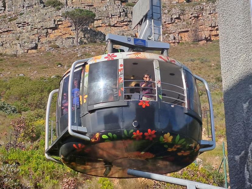 Colorful cable car ascending Table Mountain with tourists, offering scenic views on Cape Town's iconic landscape tour.