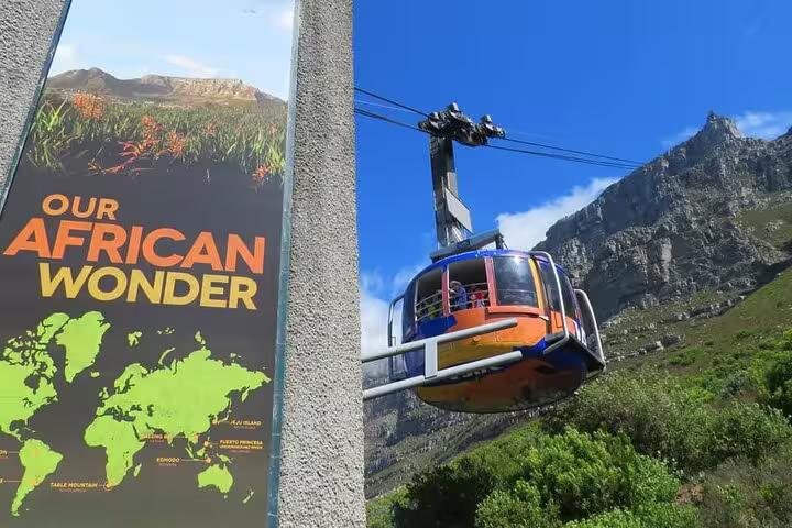 A colorful cable car ascends Table Mountain beside a sign highlighting the natural wonders of Cape Town.