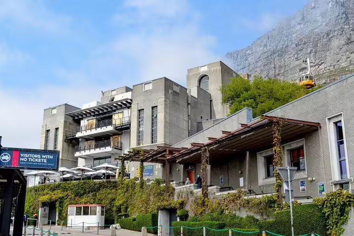 Entrance to Table Mountain cable car station, surrounded by lush greenery and dramatic mountain backdrop.