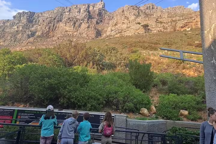 Visitors gaze at the majestic Table Mountain cliffs from the cable car station entrance on a sunny day.