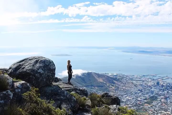 A person stands on a rocky outcrop on Table Mountain, overlooking Cape Town's breathtaking landscape and ocean vistas.