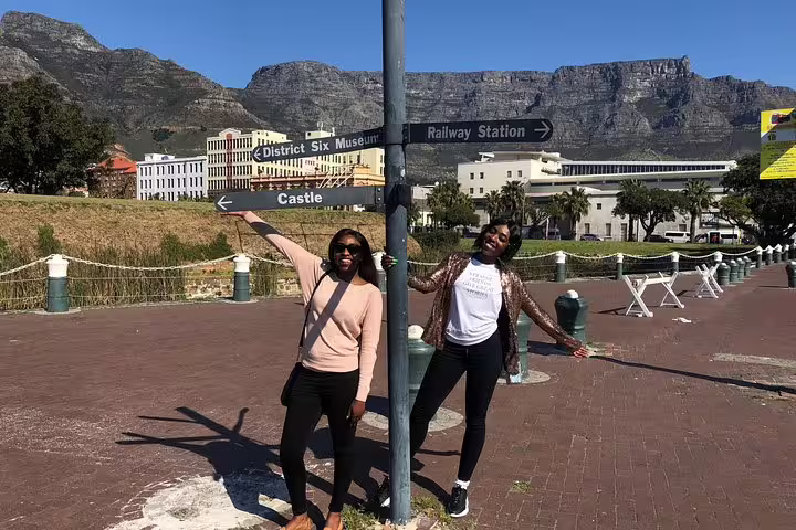 Visitors posing at a signpost near Table Mountain with directions to District Six Museum and Railway Station.