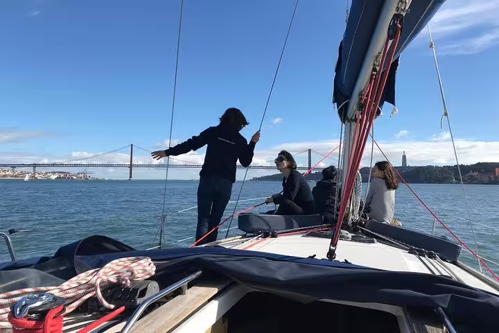 Tourists enjoy a vibrant sailing experience on the Tagus River with Lisbon's iconic 25 de Abril Bridge in the background.