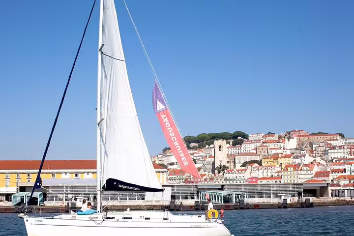 Sailboat cruising along the Tagus River with Lisbon's colorful cityscape in the background.