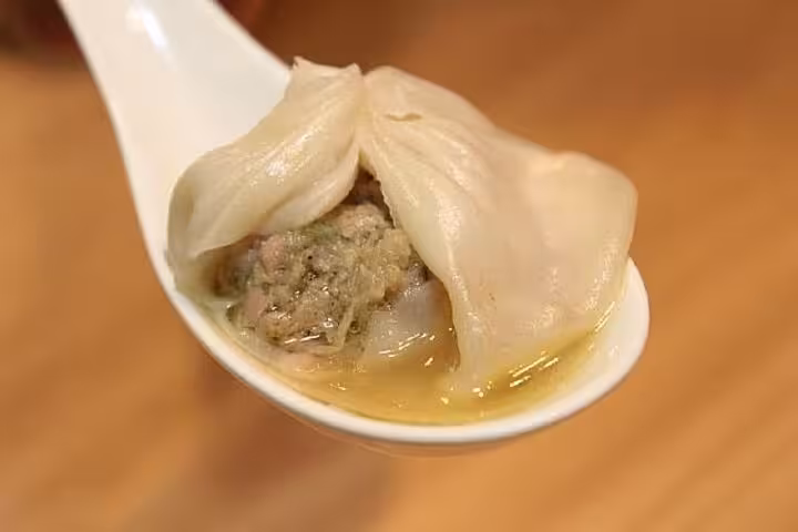 Close-up of a juicy pork xiaolongbao dumpling on a spoon at Taipei Hungzhou Xiaolongbao, showcasing rich broth and tender filling.