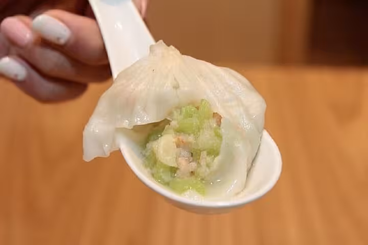 A spoon holding a fresh vegetable-filled xiaolongbao dumpling at Taipei Hungzhou Xiaolongbao, highlighting vibrant green stuffing.