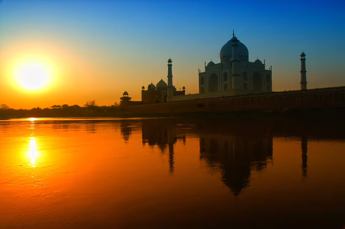 Sunset view of the Taj Mahal reflecting on the Yamuna River in Agra, highlighting classical North India beauty.