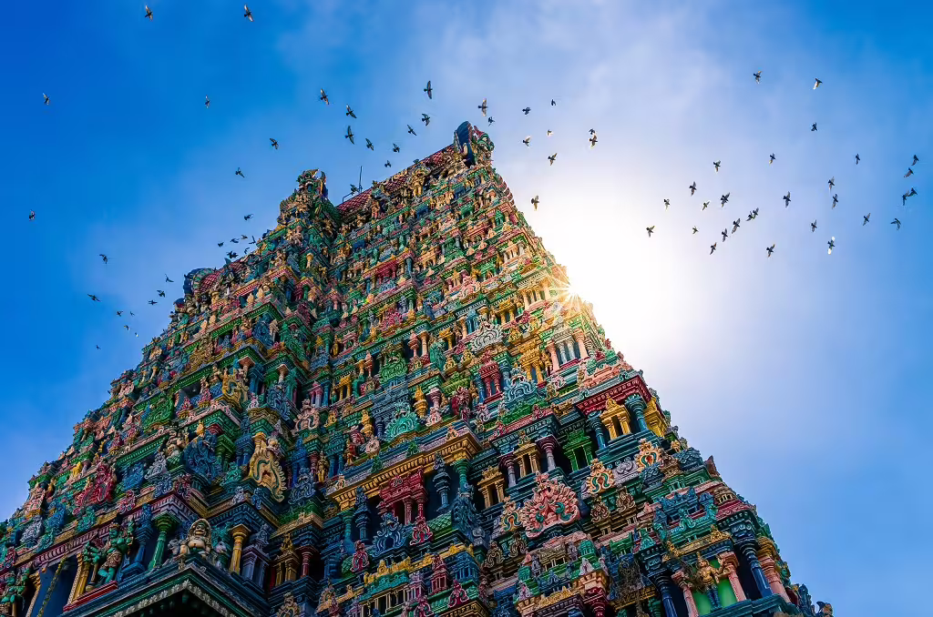 Majestic Tamil Nadu temple tower adorned with detailed carvings, birds soaring under a clear blue sky.