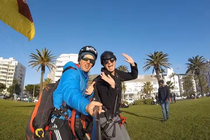 Smiling after a successful tandem paragliding landing with palm trees and buildings in Cape Town.