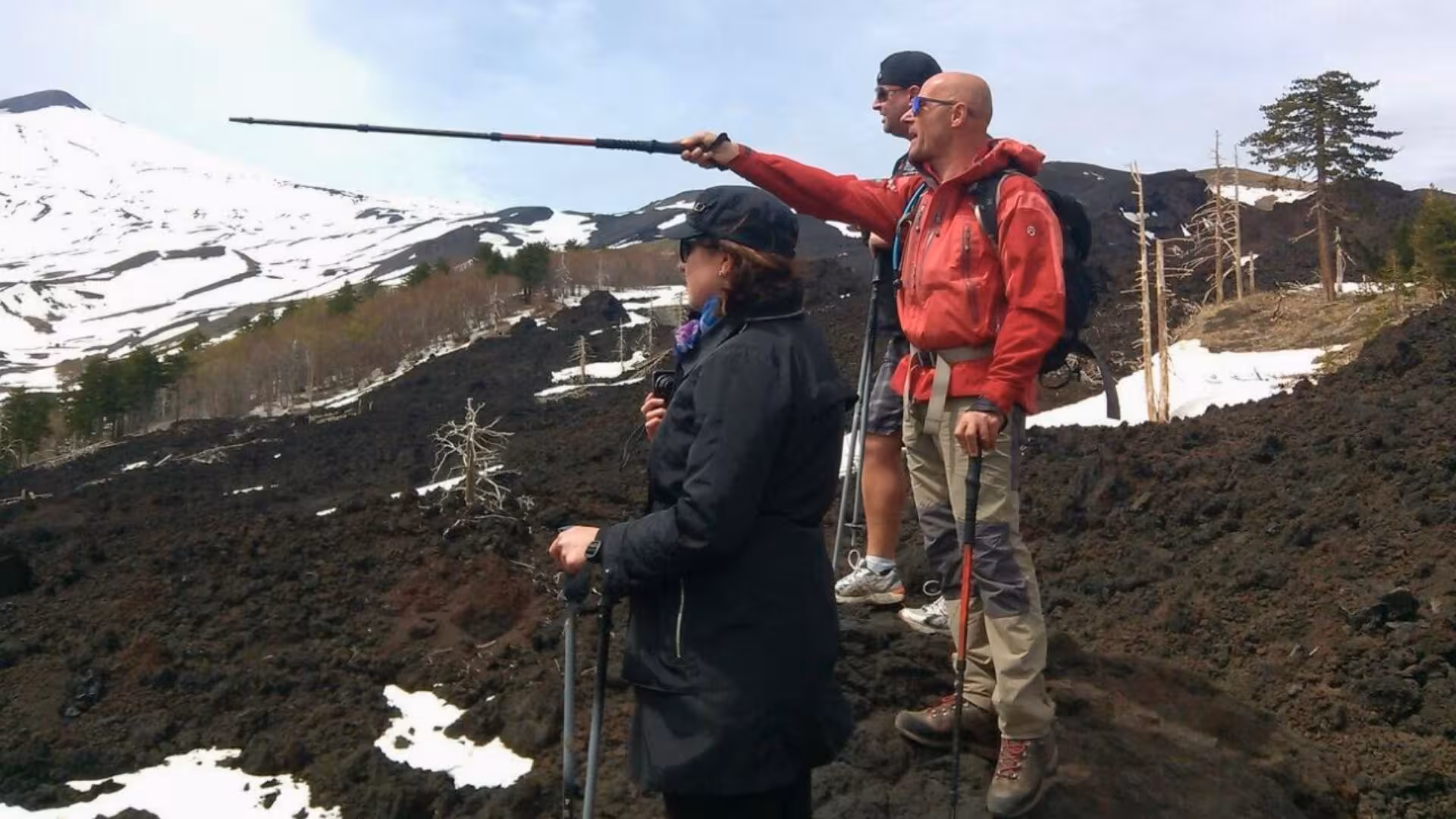 Hikers explore volcanic terrain on Mt. Etna with snow-capped peaks in Taormina, Sicily, under clear skies.