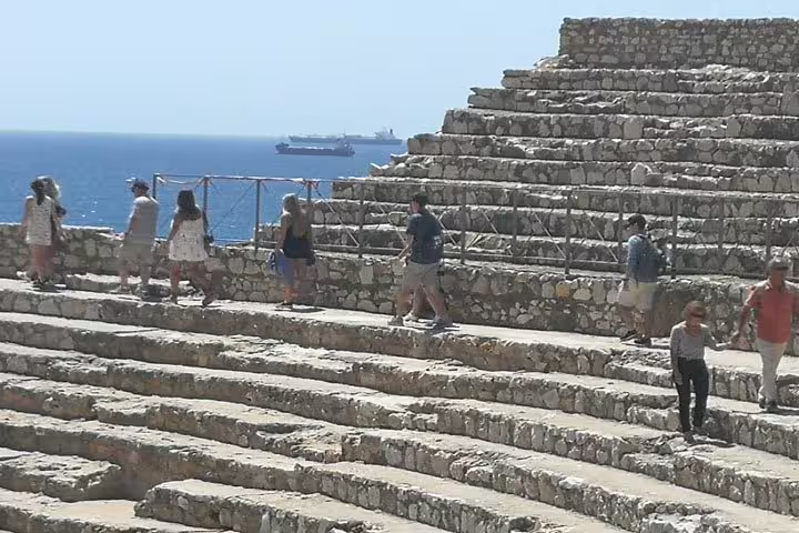 Visitors stroll through the ancient stone tiers of Tarragona's Roman amphitheater with the Mediterranean Sea in view.