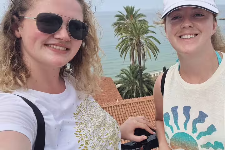 Two travelers at a Tarragona seaside viewpoint on a self-guided scavenger hunt tour, palm trees behind
